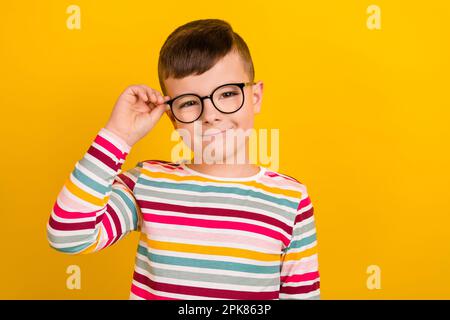 Foto eines cleveren, niedlichen Jungen gestreifte, stilvolle Kleidung Hand-Touch Brille Optik Laden leer isoliert auf gelbem Hintergrund Stockfoto