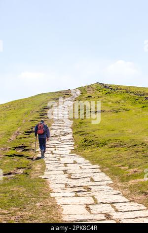 Ein Mann klettert auf die Flagsteine bis zum Gipfel des Mam Tor, dem höchsten Punkt auf dem großen Berggipfel zwischen Castleton und Hope im Peak District Stockfoto