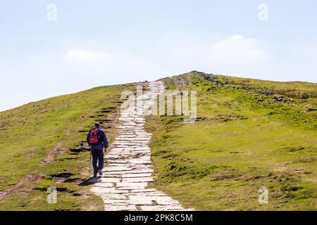 Ein Mann klettert auf die Flagsteine bis zum Gipfel des Mam Tor, dem höchsten Punkt auf dem großen Berggipfel zwischen Castleton und Hope im Peak District Stockfoto