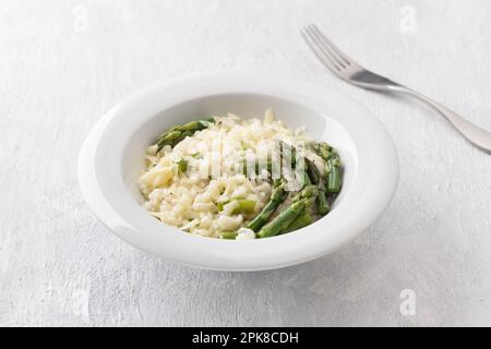Weiße Platte mit köstlichem cremigen Risotto mit Spargel und Käse auf hellgrauem Hintergrund. Traditionelle italienische Küche Stockfoto