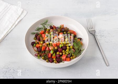 Gemüsesalat Vinaigrette mit Rüben, Kartoffeln, Karotten, Gurken, grünen Erbsen und Kräutern auf einem weißen Teller auf hellblauem Hintergrund. Traditioneller Russ Stockfoto