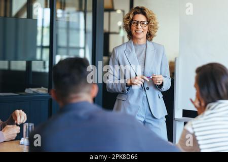 Reife Geschäftsfrau, die mit ihrem Team spricht. Frau, die ein Meeting in einem Büro leitet. Geschäftsfrau präsentiert ihre Ideen in einem Büro. Gruppe Stockfoto