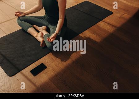 Aus dem Blickwinkel einer Seniorin, die meditiert und Hatha Yoga praktiziert. Unerkennbare Frau, die eine Atemübung macht, während sie in lockerer Pose sitzt. Wo Stockfoto