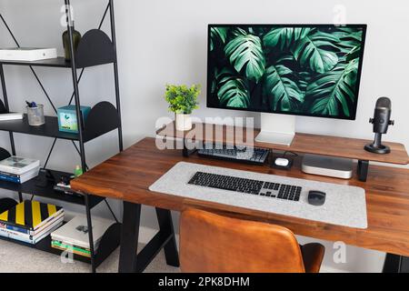 LONDON - 06. APRIL 2023: Minimaler Schreibtischaufbau in einem modernen Heimbüro mit Apple-Computertastatur, Schreibtisch aus Walnussholz und Pflanzen Stockfoto