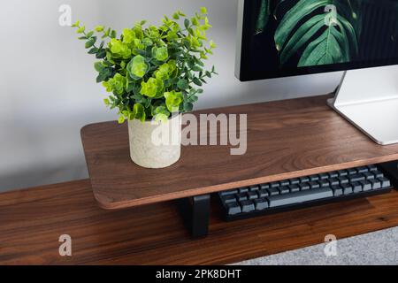 LONDON - 06. APRIL 2023: Minimaler Schreibtischaufbau in einem modernen Heimbüro mit Apple-Computertastatur, Schreibtisch aus Walnussholz und Pflanzen Stockfoto