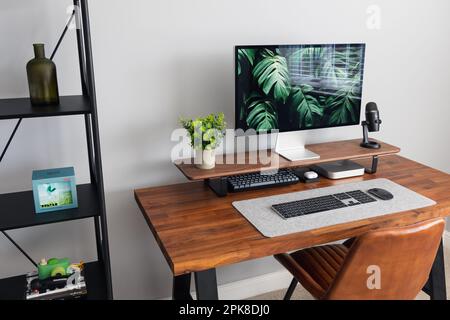 LONDON - 06. APRIL 2023: Minimaler Schreibtischaufbau in einem modernen Heimbüro mit Apple-Computertastatur, Schreibtisch aus Walnussholz und Pflanzen Stockfoto