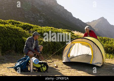 Glückliches älteres, birassisches Paar, das in den Bergen ein Zelt aufschlägt Stockfoto