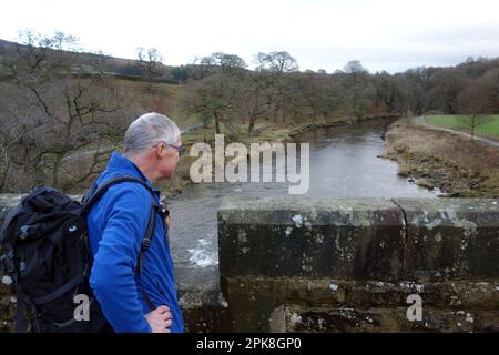 Mann, der am Dales Way National Footpath in Wharfdale, Yorkshire Dales, England, steht und über die Aqueduct/Footbridge auf der River Wharfe schaut Stockfoto