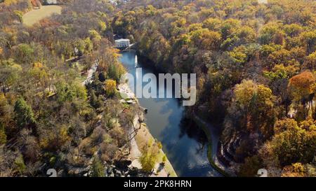 Wunderschöner Herbstpark mit Panoramablick, viele Bäume mit gelben Blättern, See mit Springbrunnen in der Mitte, Architektur, große Steine, Wege, Spazierwege, Leute, die an sonnigen Herbsttagen spazieren gehen. Draufsicht Stockfoto