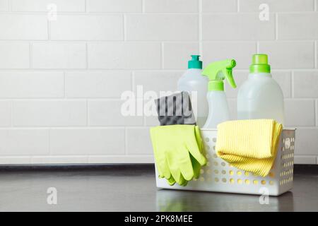 Korb mit Reinigungsmitteln, Handschuhen und Schwämmen auf dem Küchentisch. Harmloses Geschirrspülmittel. Reinigungsmittel zum Waschen von Böden. Reinigungschemikalie für den Haushalt Stockfoto