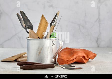 Werkzeuge zum Formen und Modellieren in einem Aluminiumbecher und einem Stück Plastik auf leichtem Werkstatthintergrund. Hobby und Kunsttag Stockfoto