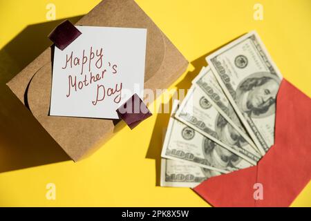 Geld in roten Umschlägen. Glückwunsch zum Muttertag Begrüßungsgeschenk, verschlossen von einem Haufen US-Dollar-Banknoten. Banknoten, die als Geschenk in einem Umschlag gefaltet wurden Stockfoto