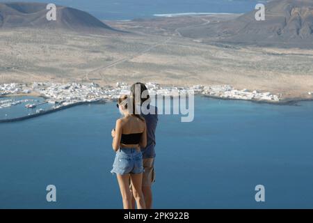 Mann und Mädchen stehen an einem Aussichtspunkt mit Blick auf die Insel La Graciosa, Kanarische Inseln Stockfoto