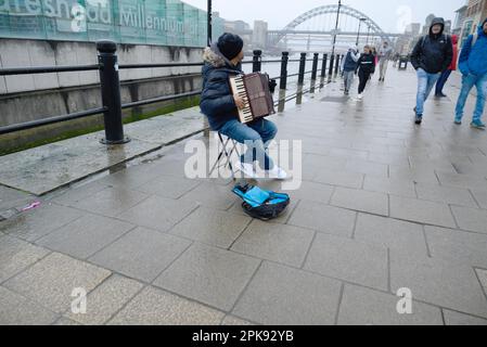 Newcastle Upon Tyne, Tyne und Wear, England, Großbritannien. Straßenmusiker spielt Akkordeon am Kai in der Nähe der Millennium Bridge Stockfoto