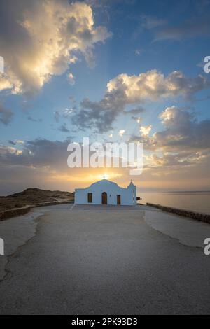 Kleine typisch griechische Kirche direkt am Meer, die weiße Agios Nikolaos Kapelle an einer felsigen Küste bei Sonnenaufgang Stockfoto