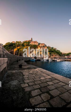 Schönes kleines Bergdorf auf der Insel Krk direkt am Meer. Sonnenaufgang mit Stadtpanorama im Hafen von Vrbnik, Kroatien. Stockfoto