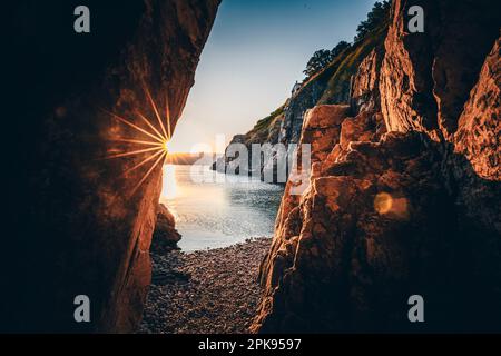 Versteckter Strand/geheimer Strand am Hafen von Vrbnik. Wunderschöne kleine Bucht umgeben von Klippen und mit einem Steinstrand. Sonnenaufgang an der Adria, Insel Krk, Kroatien Stockfoto