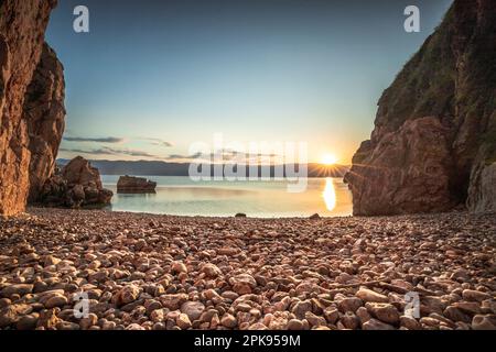 Versteckter Strand/geheimer Strand am Hafen von Vrbnik. Wunderschöne kleine Bucht umgeben von Klippen und mit einem Steinstrand. Sonnenaufgang an der Adria, Insel Krk, Kroatien Stockfoto