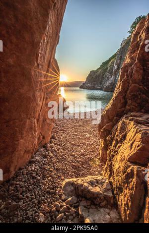 Versteckter Strand/geheimer Strand am Hafen von Vrbnik. Wunderschöne kleine Bucht umgeben von Klippen und mit einem Steinstrand. Sonnenaufgang an der Adria, Insel Krk, Kroatien Stockfoto