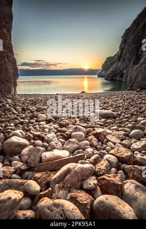 Versteckter Strand/geheimer Strand am Hafen von Vrbnik. Wunderschöne kleine Bucht umgeben von Klippen und mit einem Steinstrand. Sonnenaufgang an der Adria, Insel Krk, Kroatien Stockfoto