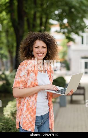 Zufriedene Freiberuflerin, die lächelt, während sie ihren Laptop benutzte und im Freien arbeitete, Stock Image Stockfoto