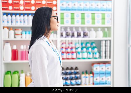 Hispanische Frau, die in einer Apotheke arbeitet und auf der Seite nach einem entspannten Profil sucht, mit natürlichem Gesicht und selbstbewusstem Lächeln. Stockfoto