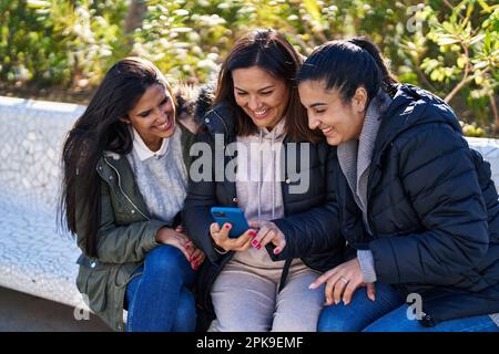 Drei weibliche Mutter und Töchter mit Smartphone sitzen auf der Bank im Park Stockfoto