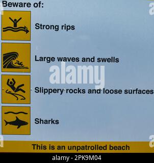 Schild an einem australischen Strand, Warnung vor starken Rissen, großen Wellen, rutschigen Felsen und Haien Stockfoto