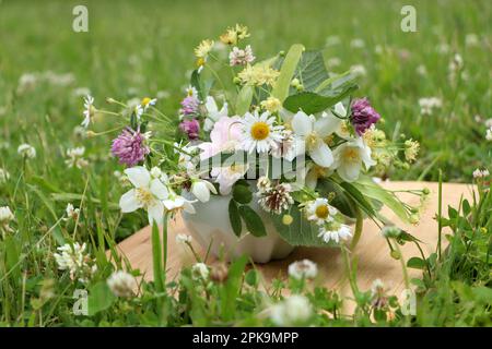 Keramikmörtel mit verschiedenen Wildblumen und Kräutern auf Holzbrettern auf der Wiese Stockfoto