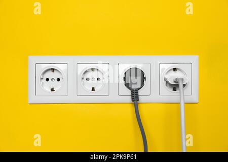 Steckdosen mit eingesteckten Steckern an der gelben Wand. Stromversorgung Stockfoto