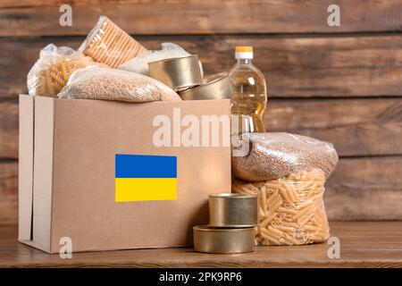 Humanitäre Hilfe für ukrainische Flüchtlinge. Spendenbox mit Essen auf Holztisch Stockfoto