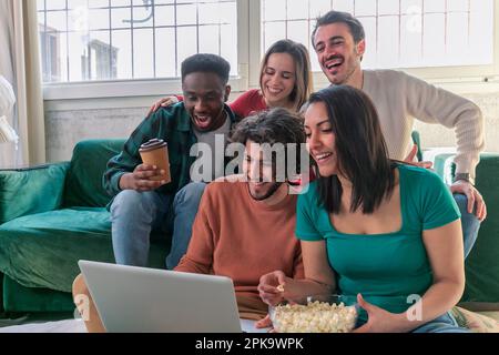 Eine Gruppe junger Freunde mit Laptop sitzt auf dem Sofa drinnen, Film zu sehen. Stockfoto