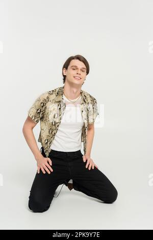 Glückliches Bigender-Modell in Bluse mit Schlangenmuster und schwarze Hose, die auf grauem Hintergrund posiert, Stockbild Stockfoto