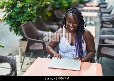 Eine afroamerikanische Frau schloss den Laptop und saß auf dem Tisch auf der Terrasse des Cafés Stockfoto
