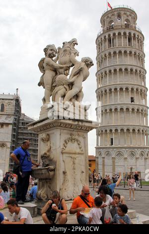 Brunnen mit Puttiskulpturen mit Cartouche, auf der Piazza dei Miracoli, Schiefer Turm im Hintergrund, Pisa, Italien Stockfoto