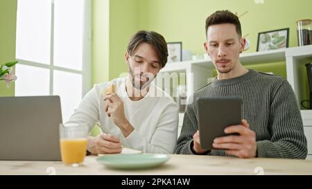 Zwei Männer, die mit Touchpad frühstücken und auf dem Notebook im Speisesaal schreiben Stockfoto