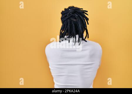 Ein afrikanischer Mann mit Dreadlocks, der einen Rollkragenpullover auf gelbem Hintergrund trägt und rückwärts mit gekreuzten Armen wegschaut Stockfoto