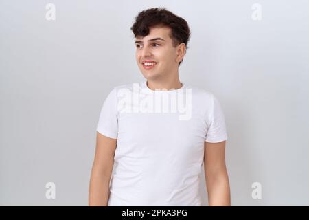 Junger, nicht binärer Mann, der ein legeres weißes T-Shirt trägt, das von der Seite wegschaut, mit einem Lächeln im Gesicht, natürlichem Ausdruck. Selbstbewusst lachen. Stockfoto