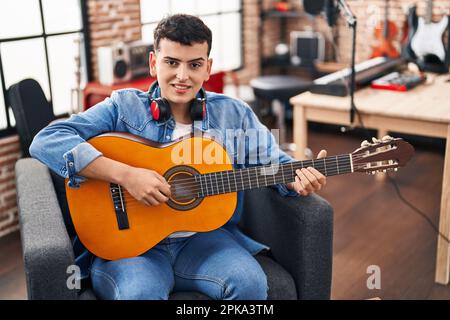 Junger nicht binärer männlicher Musiker, der klassische Gitarre im Musikstudio spielt Stockfoto