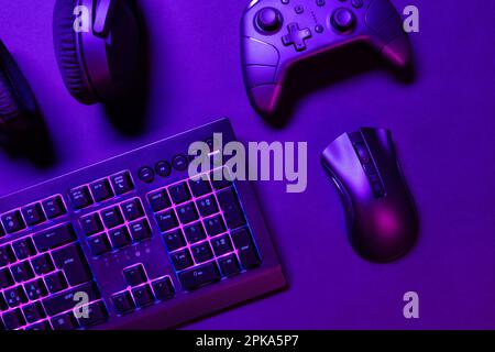 Blick von oben auf Gaming-Controller und Kopfhörer mit Maus und grün beleuchteter Tastatur auf beleuchtetem lilafarbenen Schreibtisch Stockfoto