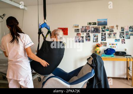 Pflegekraft bereitet die Schlafenszeit eines behinderten Patienten in seinem Zimmer im Altersheim vor. Stockfoto