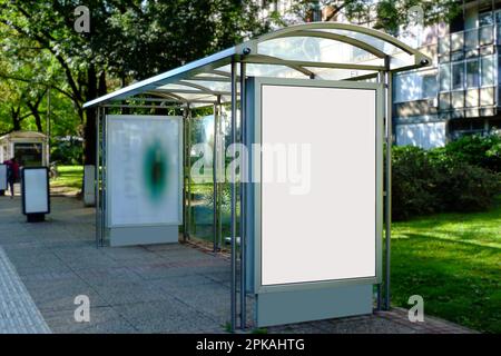 Weiße leere Anzeige und kommerzielle Reklametafel. Modellbasis. Leerer Posterhintergrund. Weicher urbaner grüner Hintergrund. Anzeigenbereich im vertikalen Format. Stockfoto