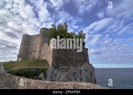 Schloss Santa Ana in Castro Urdiales mit Leuchtturm. Blauer Himmel mit sich bewegenden Wolken auf der Flucht, ruhiges Meer, steinige Straße Stockfoto