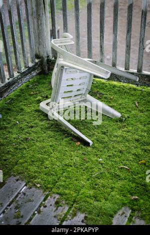 Heruntergefallener Plastikstuhl auf moosem Teakboden eines Balkons Stockfoto