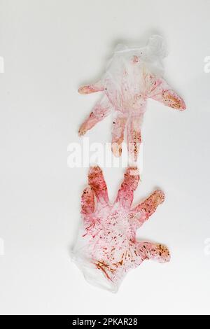 Rot verfärbtes Paar Einweghandschuhe auf einer weißen Oberfläche Stockfoto