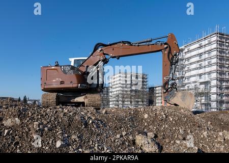 Der braune Hydraulikbagger steht auf einer großen Baustelle mit mehrstöckigen Muschelbauten im Hintergrund Stockfoto