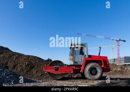 Rote Rollenständer auf einer großen Baustelle vor dem Erdhaufen mit Baukränen im Hintergrund Stockfoto