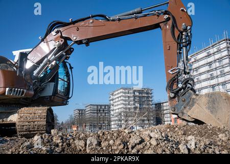 Der braune Hydraulikbagger steht auf einer großen Baustelle mit mehrstöckigen Muschelbauten im Hintergrund Stockfoto