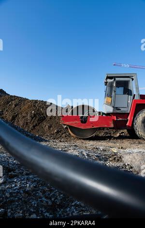 Rote Rollenständer auf einer großen Baustelle vor dem Erdhaufen mit Baukränen im Hintergrund Stockfoto