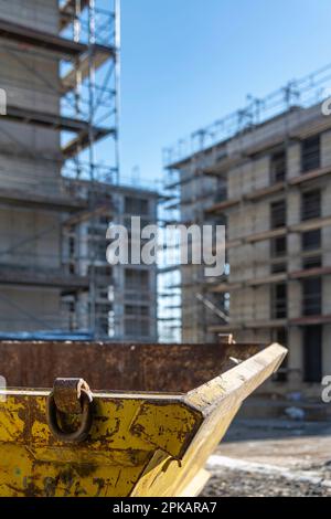 Ein gelber Behälter für Bauabfälle steht auf einer Baustelle vor Gerüstbauten im Hintergrund Stockfoto